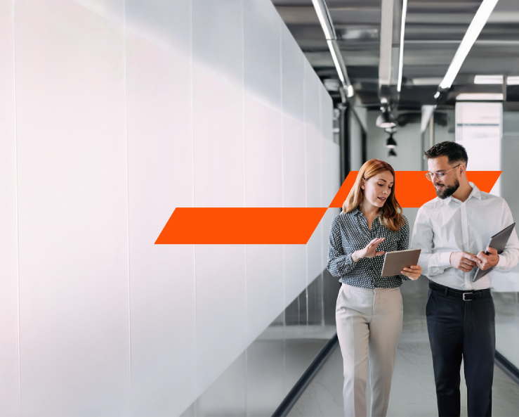 Two office mates discussing work in a modern office next to walls covered in white frosted glass, glowing on their left. 
