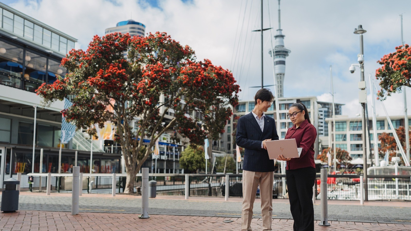 Two colleagues standing along the Auckland Viaduct. The Sky Tower is in the background. 