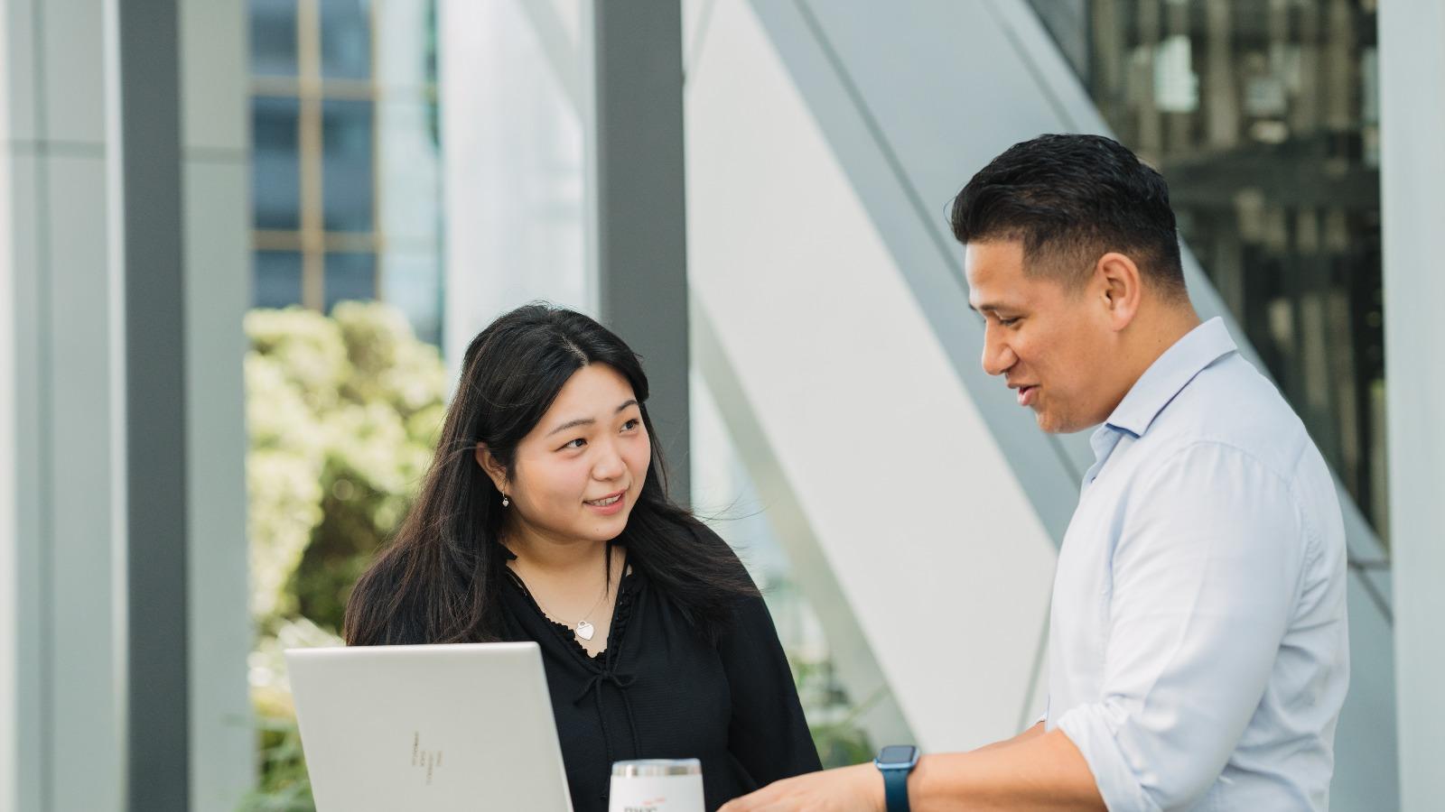Two young professionals having a meeting in an outside space by a modern office.