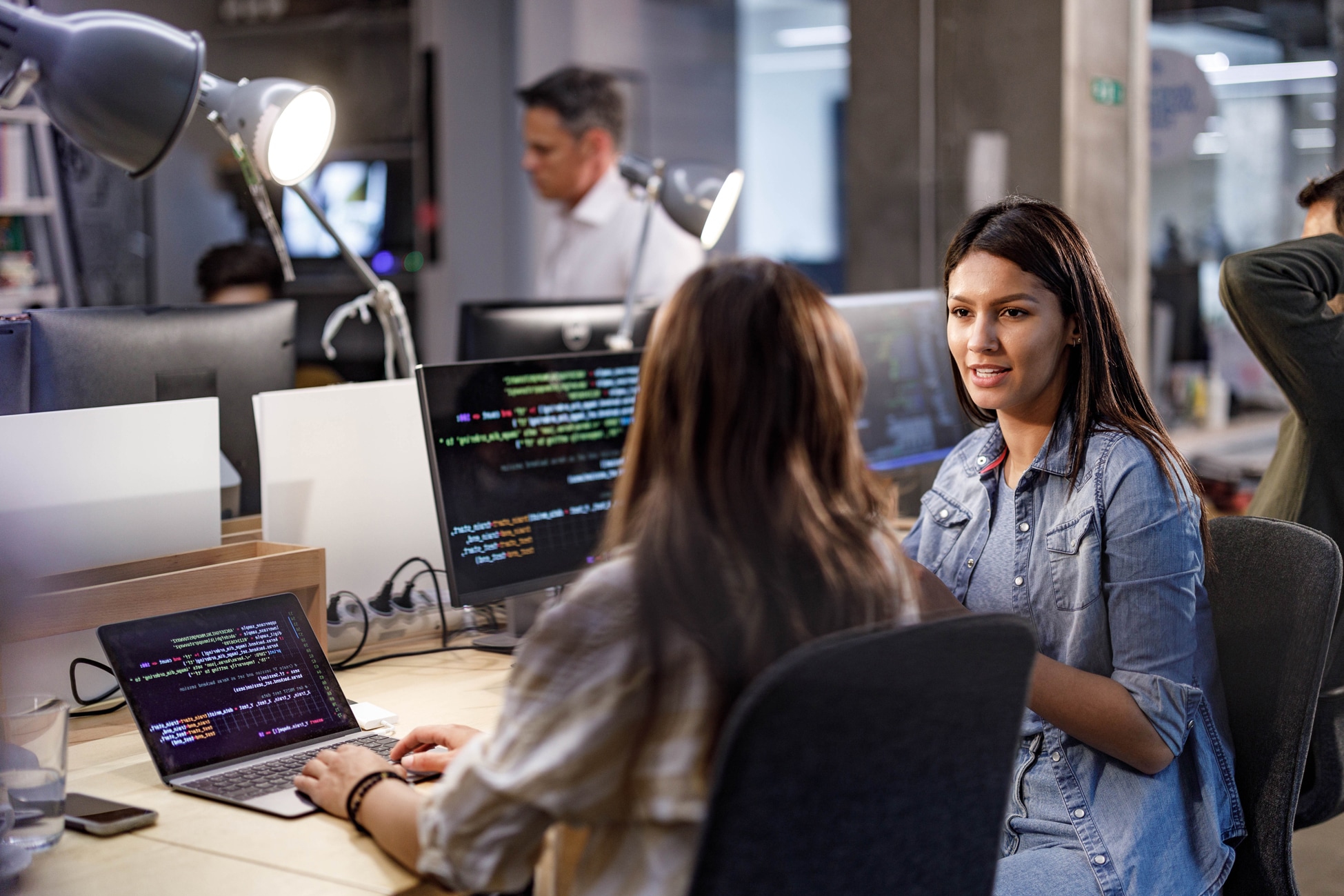 Two colleagues speaking with each other next to computer screens.